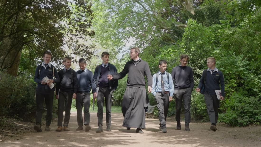 Un prêtre et des élèves marchant ensemble dans une allée du parc