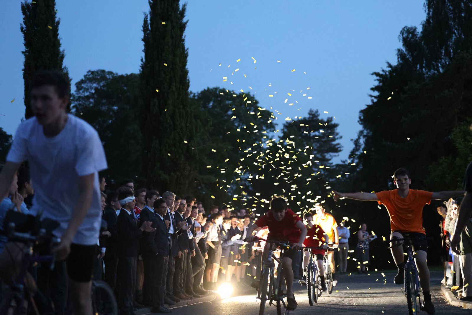 Course de vélos au crépuscule sous les confettis, encouragée par les élèves