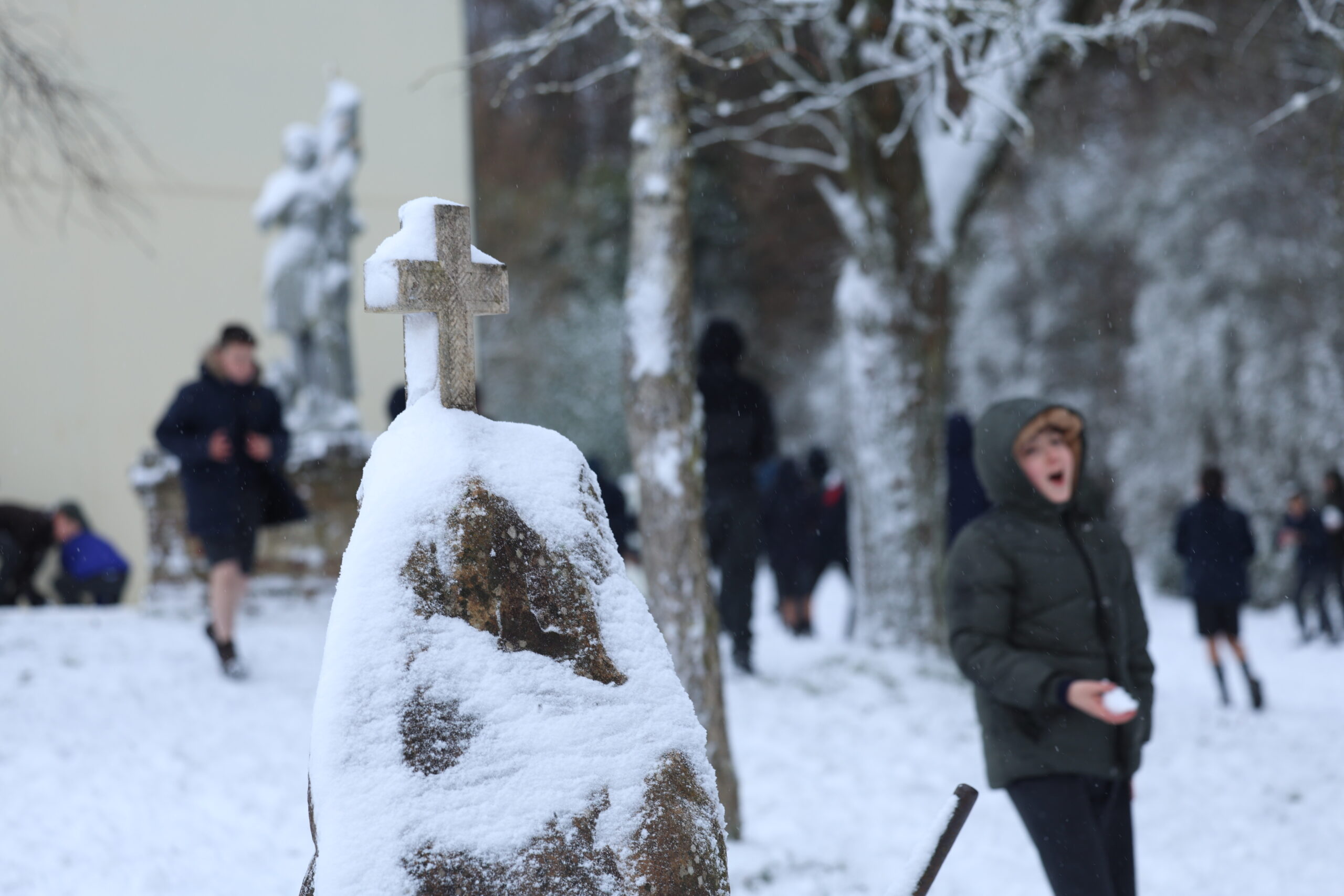 Élèves jouant dans la neige près d’une croix de pierre enneigée