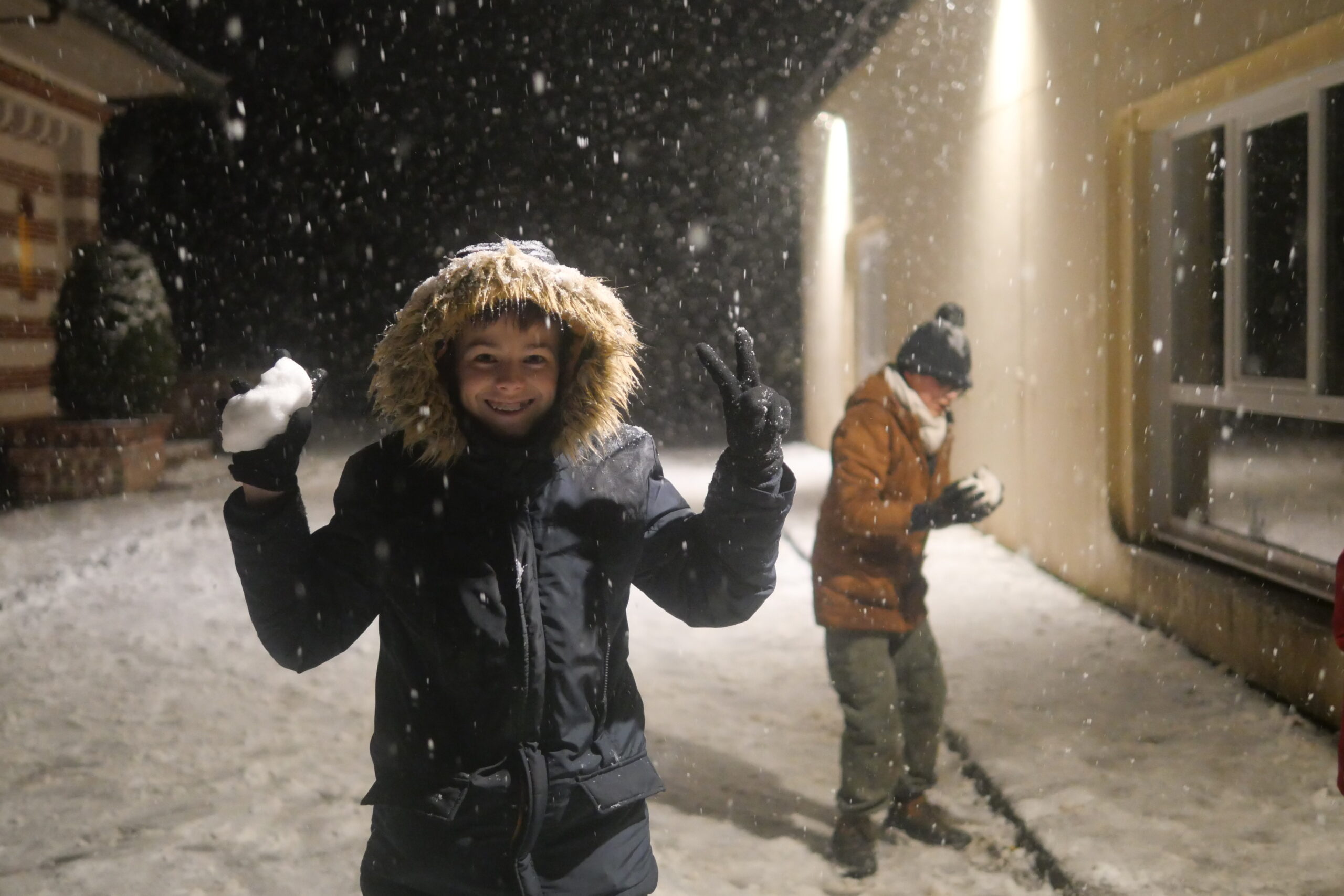 Élève faisant le signe de la victoire, une boule de neige à la main, sous la neige de nuit